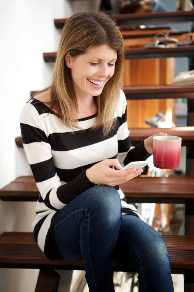 caucasian woman sitting on stairs and using smart phone at home
